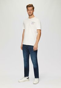 T-shirt blanche avec un petit motif imprimé, associée à un jean bleu foncé et des baskets blanches. Coupe décontractée et manches courtes.