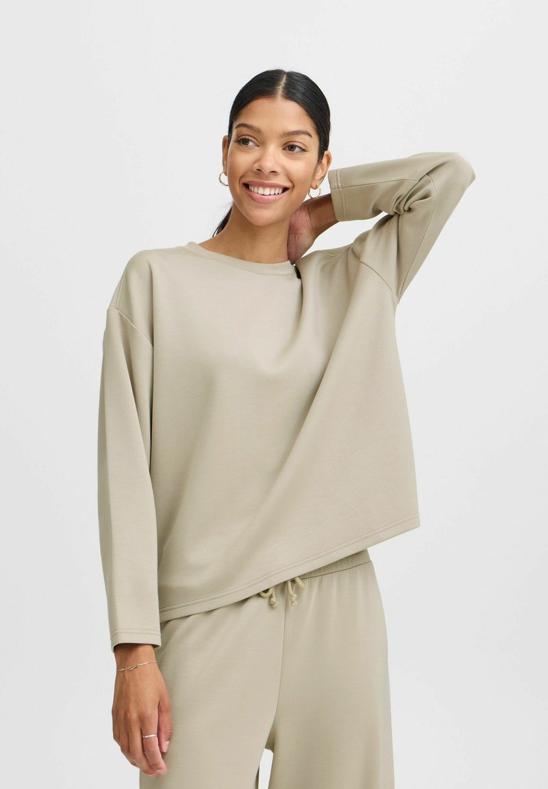 Beige oversized sweatshirt med rund halsudskæring og lange ærmer, lavet af et glat stof. Har en afslappet pasform og diskrete sømdetaljer.