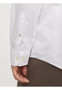 Camisa blanca de manga larga con puños abotonados de dos botones y tejido texturizado. La camisa tiene un dobladillo recto.