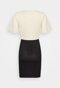 Mekko, jossa on teksturoitu kermahiha ja istuva musta hame, joka sisältää liehuvia hihoja ja pyöreän pääntien. Sopii muodollisiin tilaisuuksiin.