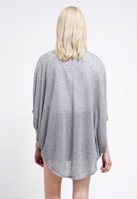 Maglione grigio largo con maniche ampie, texture morbida e orlo arrotondato. La vista posteriore mostra una silhouette rilassata e una leggera caduta.