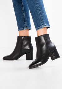 Schwarze Lederstiefeletten mit spitzem Zehenbereich, glatter Oberfläche, Seitenreißverschluss und stabilen Absatz, kombiniert mit cropped blauen Jeans.