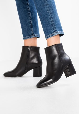 Zwarte leren enkellaarzen met een puntige neus, een gladde textuur, een rits aan de zijkant en een chunky hak, gecombineerd met cropped blauwe denim jeans.