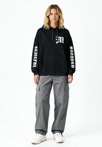 Felpa nera con grafica bianca e tasca frontale ampia, abbinata a pantaloni cargo grigi con tasche laterali e polsini elastici.