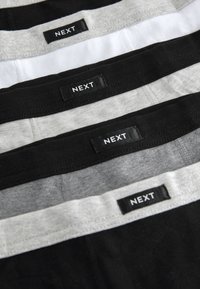 Quatre paires de sous-vêtements pour hommes en noir, gris et blanc. Chacune comporte une ceinture élastique douce avec l'étiquette "NEXT" bien visible.