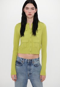 Lime green cropped cardigan with button closure and four front pockets; ribbed cuffs and hem; paired with light blue jeans.