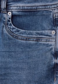 Vaqueros de mezclilla con un tono azul, que presentan un bolsillo delantero, costuras estándar y un adorno de remache metálico redondo cerca del bolsillo.