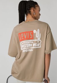 Beige cotton t-shirt featuring a graphic print in red and white, displaying "Levi's Authentic Western Wear" and a cactus design.