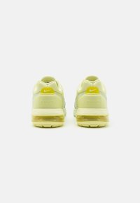 Baskets Nike avec un design jaune clair et gris, tige en maille et semelle avec amorti transparent, avec un petit accent jaune sur le talon.
