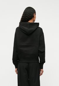 Μαύρο cropped hoodie φτιαγμένο από μαλακό ύφασμα, με κουκούλα και ριχτές μανσέτες, φαίνεται από την πλάτη με λευκό φόντο.