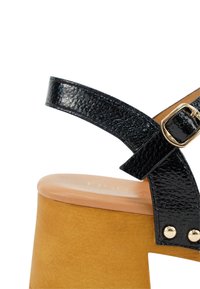 Zwarte leren hooggehakte sandaal met een gestructureerd oppervlak, voorzien van een brede band en gouden gesp-details, gemonteerd op een tan platform.
