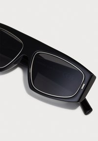 Schwarze rechteckige Sonnenbrillen mit dunklen Gläsern, silbernen Akzenten am Rahmen, glattem Plastikmaterial und glänzender Oberfläche.