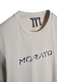 Camiseta de color beige claro, hecha de algodón y con cuello redondo. Presenta un estampado gráfico de "MORATO" en tonos oscuros en la parte frontal.