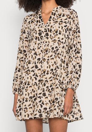 Donna che indossa un vestito lungo a maniche lunghe con stampa leopardata, scollo a V e balze arricciate, in piedi con le braccia rilassate ai lati.
