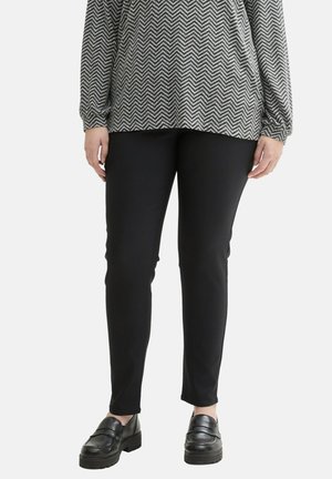 Černé slim-fit kalhoty s ribovanou texturou, doplněné šedým a bílým topem se zvlněným potiskem. Černé mokasíny outfit dokončují.