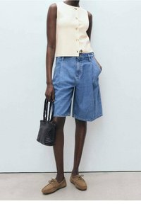 Cremfarbene ärmellose Bluse mit Knöpfen, blaue Denim-Shorts, braune Schnürschuhe und eine kleine schwarze geflochtene Tasche. Glatte Textur, lässiges Design.