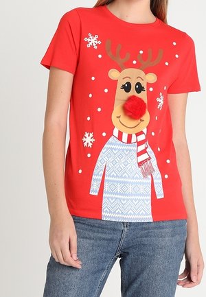 Henkilö, jolla on päällään punainen t-paita, jossa on hymyilevän poron kuva, punainen tupsunenä, huivi ja valkoisia lumihiutaleita ympärillään.
