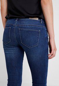 Jeans skinny azul oscuro de denim, con un diseño clásico de cinco bolsillos, una textura lisa y un ligero desvanecimiento en los muslos.