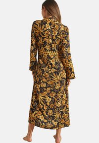 Lang zwarte jurk met levendige gele bloemenpatronen, met lange mouwen, een getailleerde taille en een vloeiende snit.