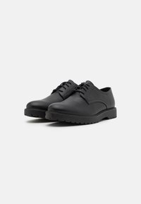 Scarpe in pelle nere con punta arrotondata, tacco basso e lacci arrotondati, caratterizzate da una suola texturizzata e un design minimalista.