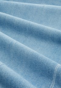 Ljusblå denimtyg med en texturerad yta, som visar synliga vävningar och veck, och har en slät, mjuk finish.