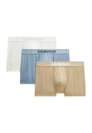 Trzy pary męskich bokserek w kolorach beżowym, niebieskim i białym z gumkami z logo "lululemon", ułożone na siebie.