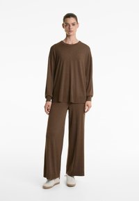 Maglia marrone a maniche lunghe in maglia con spalle scese abbinata a pantaloni a gamba larga, entrambi di una tonalità coordinata, indossati con sneaker color crema.