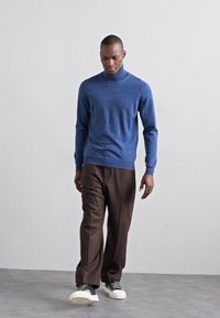 Blå høyhalset genser kombinert med brune pinstripede bukser og hvite joggesko. Jevn tekstur, tettsittende design, uformell stil.