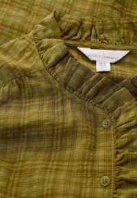 Blouse à carreaux verts avec un col à volants, une fermeture à boutons et un tissu doux et texturé. L'étiquette indique "Seasalt Cornwall".