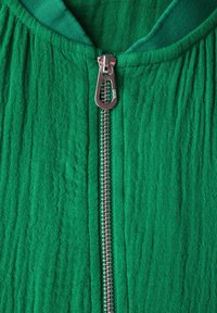 Groene zip-up kledingstuk met een gestructureerde, gekreukte stof. Heeft een zilveren metalen ritssluiting en een zachte, effen kraag.