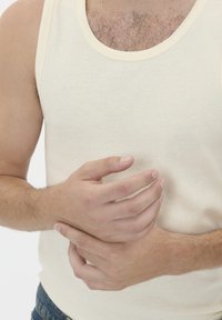 Bėrinių smėlio spalvos liemenė su kreminės spalvos apykakle, atskleidžianti plaukuotą krūtinę. Rankos sujungtos natūralioje pozicijoje prieš baltą foną.