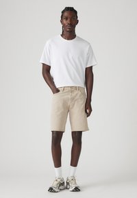 Shorts din denim bej cu o croială lejeră, asorta�ți cu un tricou alb simplu. Întregul ansamblu este completat cu adidași gri și albi și șosete albe.