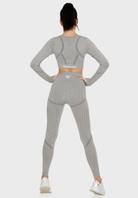 Gray long-sleeve crop top and high-waisted leggings with textured patterns and cutouts, paired with white athletic shoes.