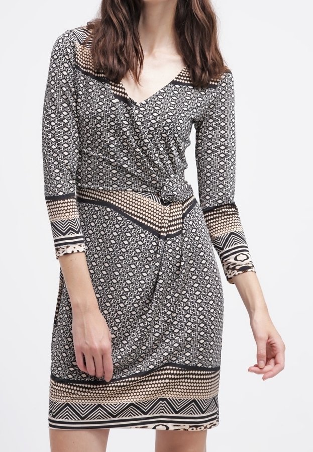 Femme portant une robe portefeuille à motifs noir et blanc avec des manches trois-quarts et des motifs géométriques en bordure.