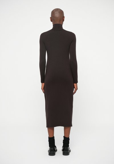 Rjava dolga majica s turtleneck ovratnikom, oprijet kroj, dolžina do sredine meč, gladka tekstura, v kombinaciji s črnimi nogavicami in čevlji.