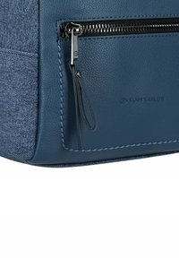 Borsa a tracolla blu con un pannello di denim testurizzato e pelle liscia. Presenta una cerniera metallica, dettagli di cucitura e un logo impresso sul lato.