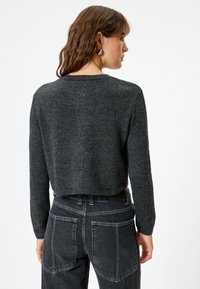 Maglione grigio corto con maniche lunghe, texture a maglia e scollatura rotonda. Abbinato a jeans neri a vita alta con grandi tasche posteriori.