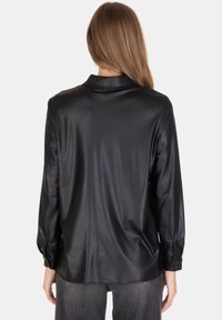 Camicia in ecopelle nera con colletto, maniche lunghe e polsini con bottoni, caratterizzata da una texture liscia e una vestibilità comoda.