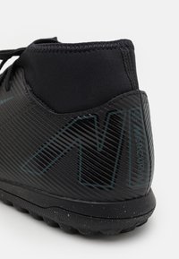 Czarny but sportowy z fakturowaną powierzchnią i pionowymi paskami, w wyższym fasonie oraz w spodzie w plamki. Akcentowany logo.