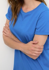 T-shirt en coton bleu à manches courtes et encolure ronde. Texture lisse et coupe décontractée, mettant en valeur l'épaule et le bras.