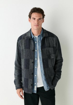 Plaid jacket in dark gray wool blend, featuring a collared neck, button front, textured fabric, and two front pockets over a denim shirt.