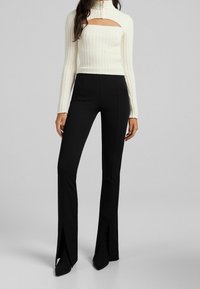 Vit ribbade tröja med hög hals och fyrkantig urskärning, kombinerad med svarta figurnära byxor med utsvängda ben och sprund vid fållen.