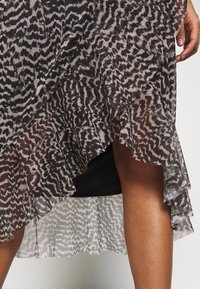 Abito fluido a strati con un tessuto trasparente caratterizzato da un motivo animalier in nero e beige. L'orlo arricciato aggiunge textura e movimento.