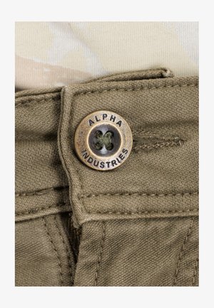 Tkanina w oliwkowym kolorze o teksturowanym wykończeniu, z brązowym guzikiem wygrawerowanym napisem "ALPHA INDUSTRIES" oraz kontrastowym nicią do szycia.