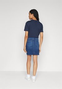 Navy t-shirt with short sleeves paired with a denim mini skirt. The skirt features two rear pockets and a straight cut, worn with white sneakers.