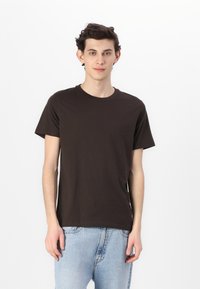 Brun bomull T-skjorte med rund hals og korte ermer, sammen med lyseblå denimjeans med avslappet passform.