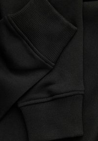 Gros plan sur les poignets d'un sweat-shirt noir montrant le tissu en maille côtelée et les détails des coutures.