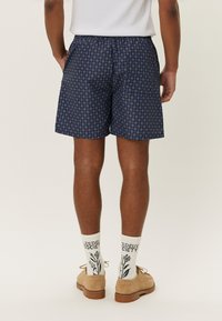 Pantaloni scurți cu un model marinăresc, având un design circular, cu un tiv elastic și două buzunare laterale. Asortează-i cu pantofi bej și șosete albe cu model.