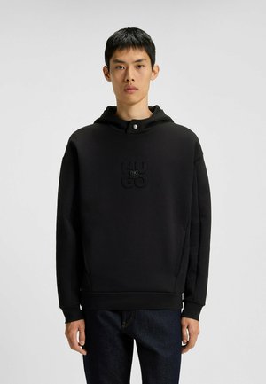 Felpa nera con cappuccio realizzata in tessuto morbido, con logo frontale, cappuccio grande e maniche lunghe, abbinata a pantaloni in denim scuri.