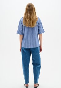 Blårandig kortärmad skjorta med lös passform, kombinerad med högmidjade blå jeans. Tyget verkar texturerat och avslappnat.